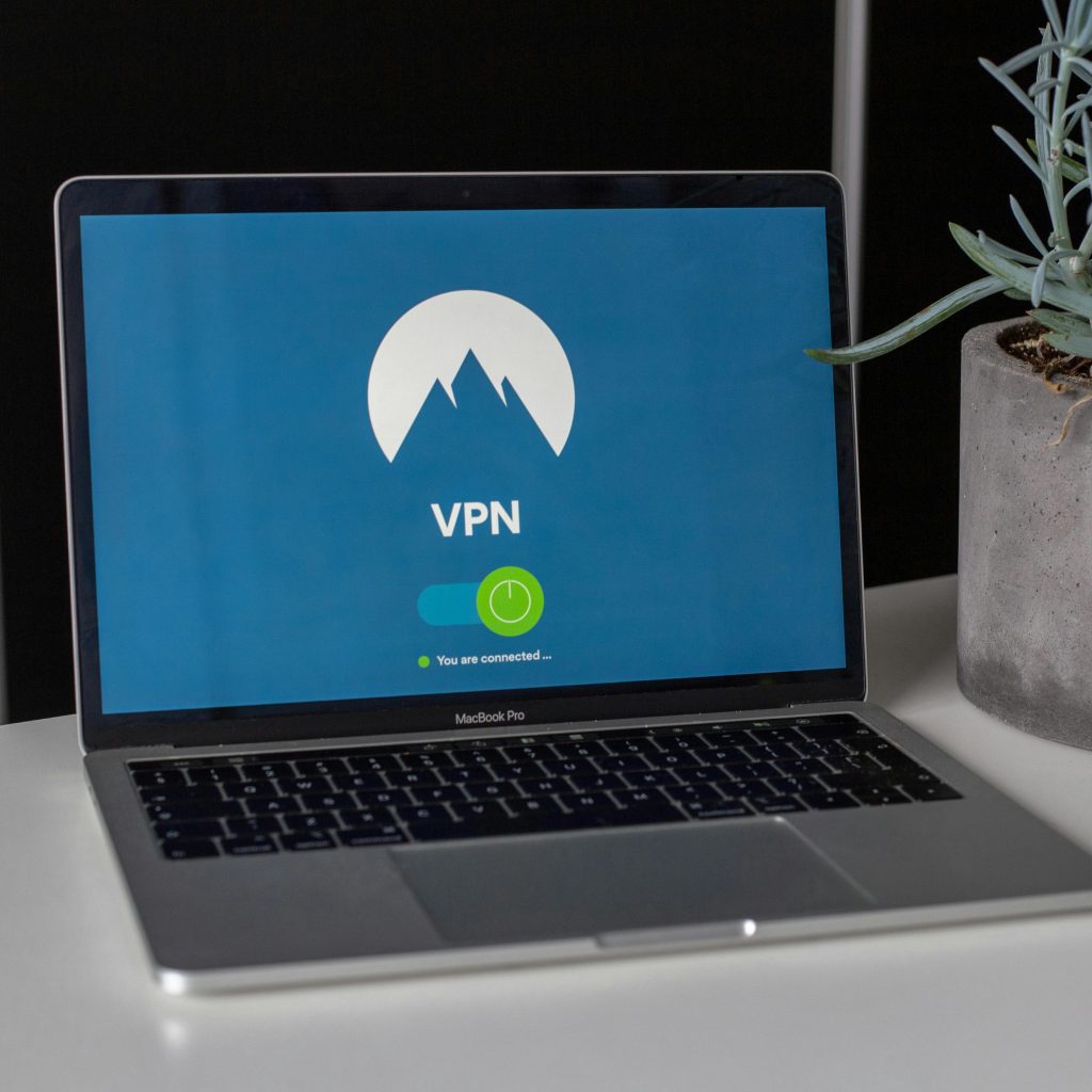 a macbook computer on a desk, with a white vpn logo on a blue background. There is a green switch, saying “you are connected”.