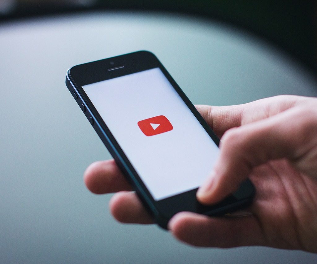 A hand holding a phone with a white background and a Youtube logo visible on the screen